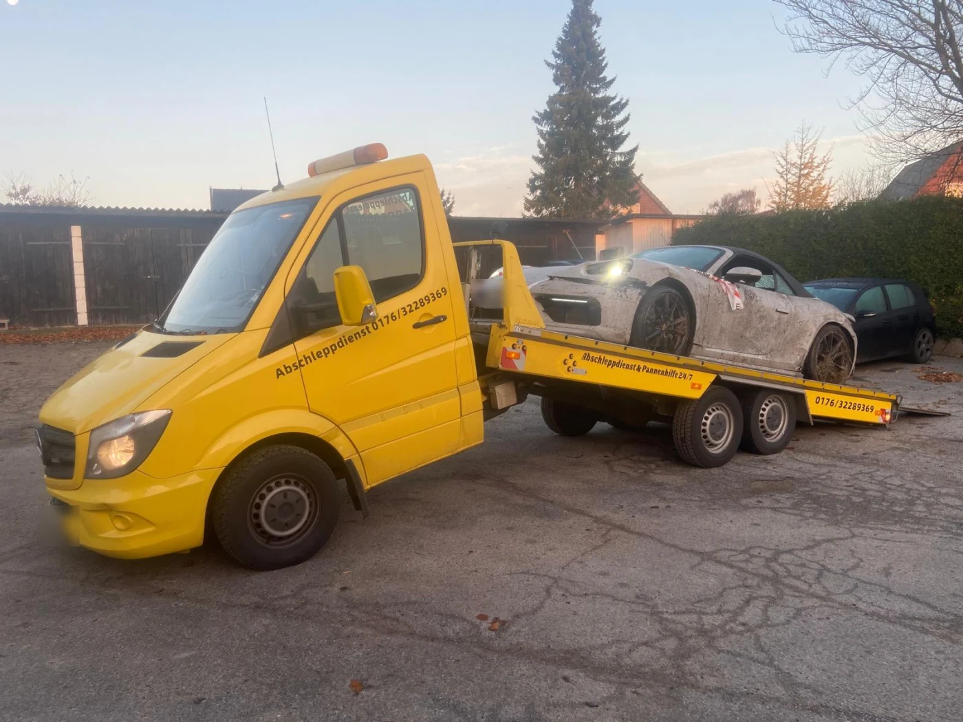 Beschädigter Sportwagen bei Dämmerung auf dem Abschleppwagen